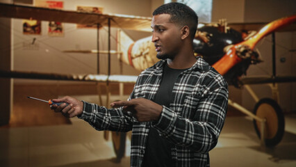 Man holding screwdriver pointing finger in building with biplane exhibit and wooden propeller visible, gesturing repair work  instructional confidence. © Krakenimages.com