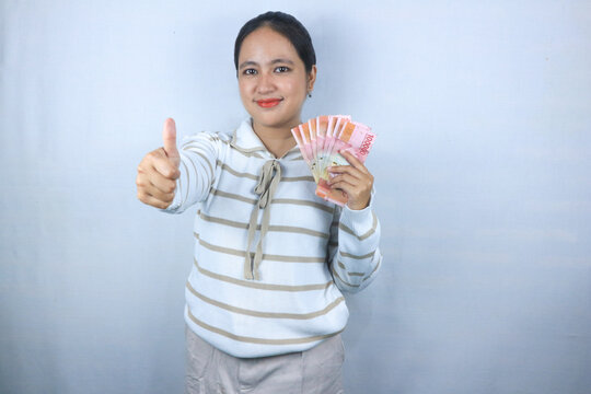 Beautiful asian woman in sweater hold indonesian banknote giving thumps up gesture