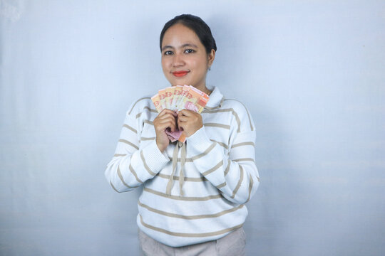 Beautiful asian woman in sweater hold indonesian banknote, isolated on white background