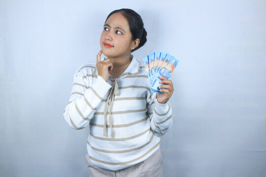 Beautiful asian woman in sweater thinking something while holding money isolated on white background
