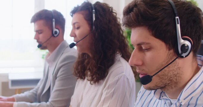 Customer support operators team with headset working in office. Serious busy call center and helpdesk agents sitting in row to explain information, technical service staff talking to clients on phone