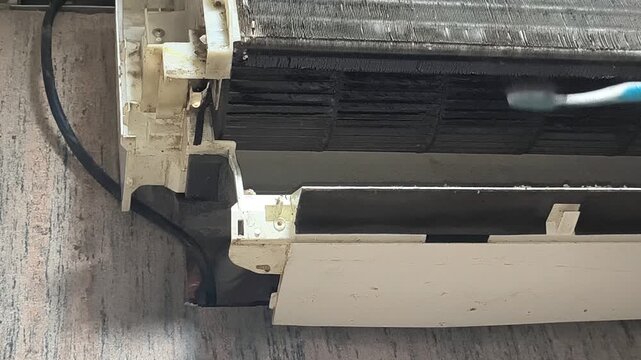 HVAC technician performing split AC filter maintenance and cleaning in indoor setting with careful inspection. Professional appliance servicing footage showing essential cooling system care