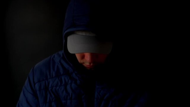 Hooded shadowed person. A man in the dark in a hood and baseball cap hides his face from outsiders. High quality FullHD footage
