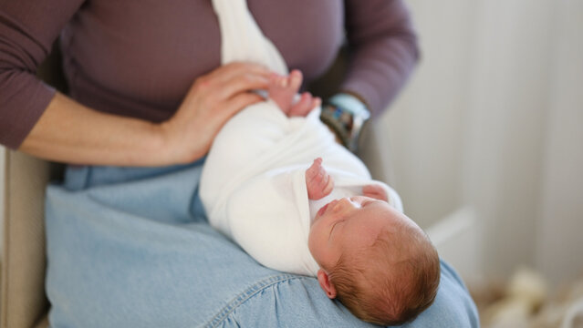 Mom Adjusts Wrap Around Newborn Baby While Sitting Indoors.