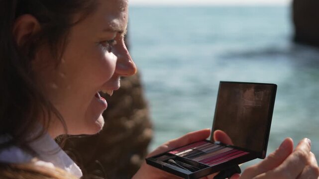Skincare serum beach woman applying facial oil looking in mirror during refreshing outdoor beauty routine on sunny day