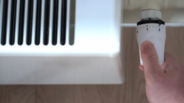 Hand adjusting a thermostatic radiator valve from level 1 to 0. Concept of heating control, energy efficiency, heating season and comfortable home temperature regulation. High quality FullHD footage