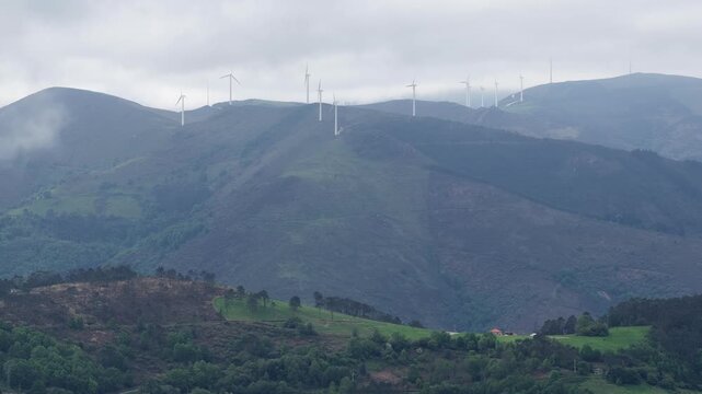 Aerial view of wind turbines on green mountain ridges under a misty sky in Asturias, Asturias, Spain.