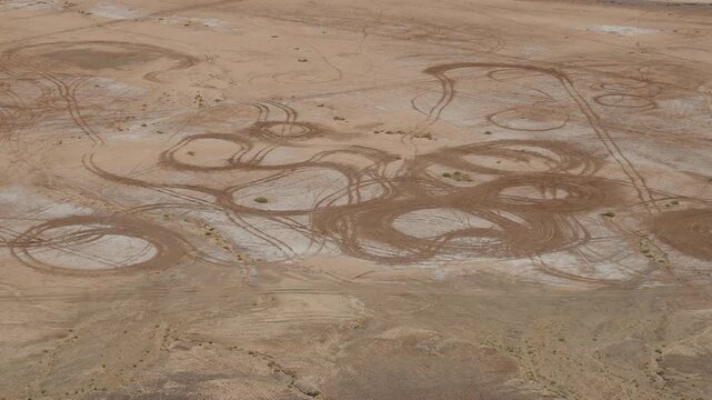 View from cliff top of Gara Medouar over cracked flat desert ground covered in overlapping circular vehicle tracks and erosion rings