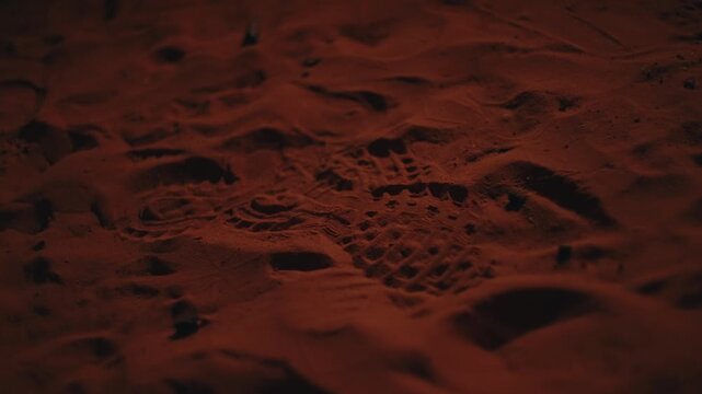 Sahara sand surface with deep shadows and footprints illuminated by red orange flickering firelight at night