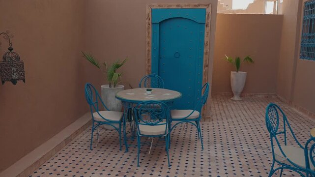 Traditional riad courtyard with blue metal table and chairs on zellige floor with blue wooden door and potted plants