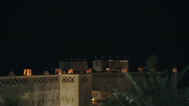 Traditional mud brick kasbah with glowing windows and decorative walls under dark night sky