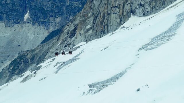 Cinematic aerial video of the Aiguille du Midi cable car in Chamonix, France. Scenic view of gondola transport over snow-covered alpine mountain peak and glacier in the French Alps