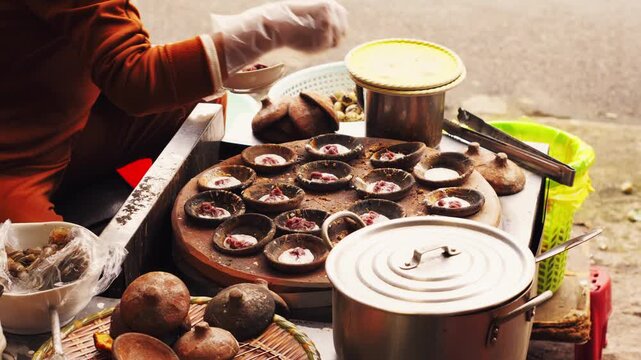 A street vendor prepares authentic Vietnamese mini pancakes (Banh Can) in traditional clay molds. A delicious look at local Asian street food culture and cuisine