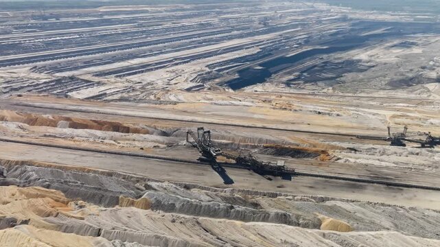 Gigantic excavation machines working in a vast open-cast coal mine on sunny day, aerial orbit