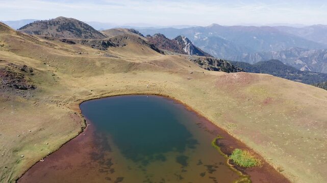 Backwards reveal drone shot of Drakolimni, Dragon Lake Smolikas on Mount Smolikas under a clear sunny sky