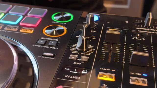 Hand of a DJ adjusting a fader on a professional mixing console during a live music performance with glowing buttons.