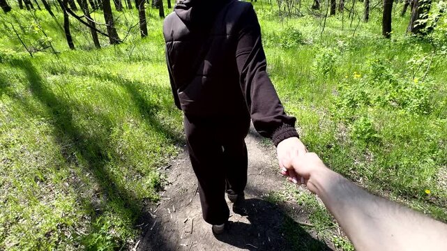 "Follow me" concept. POV video of a happy couple hiking in spring woods. Girl in a vest leads a guy by the hand, then walks forward to enjoy the view. Adventure and togetherness
