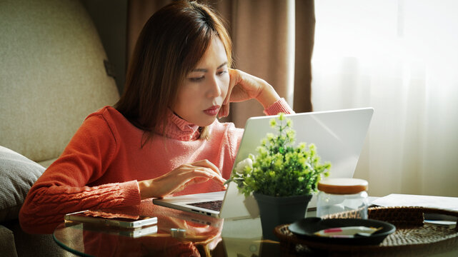 Asian woman communicating in online meeting while working from home with laptop and cozy interior background