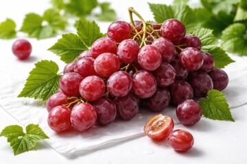 Naklejka premium Red globe grapes paired with green leafy sprigs arranged on a crisp white setting featuring vivid color and detailed texture