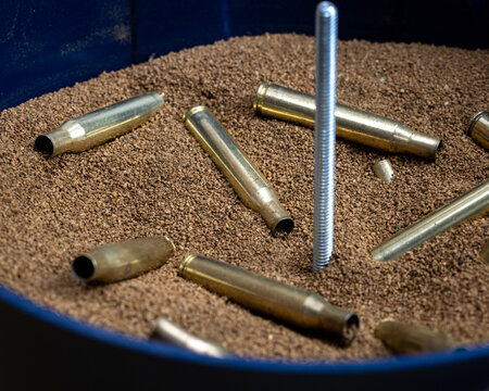 Brass shell casings tumbled in a vibratory finisher with media and a metal rod