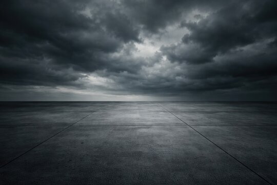 Minimalist dark concrete floor panel with dramatic cloud covered gray sky and horizon copy space