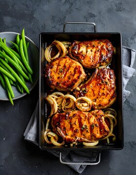 Glasierte Schweinekoteletts mit Schalotten, in einer Backform angerichtet mit gr&uuml;nen Bohnen.