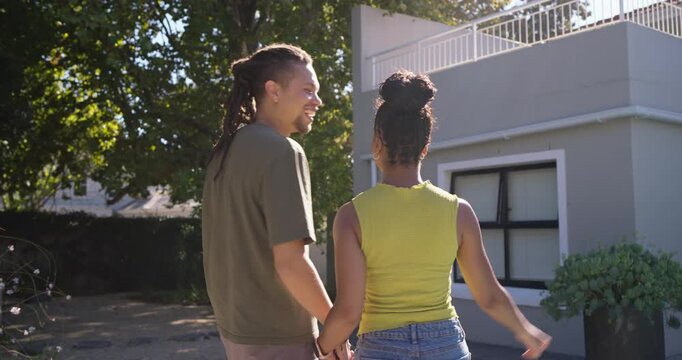 African American couple at driveway, woman pointing at balcony, presenting red key fob celebrating