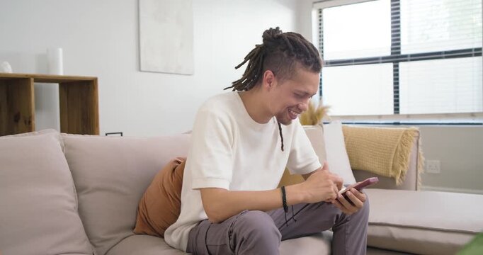 African American man scrolling smartphone on couch in living room reacting to funny message