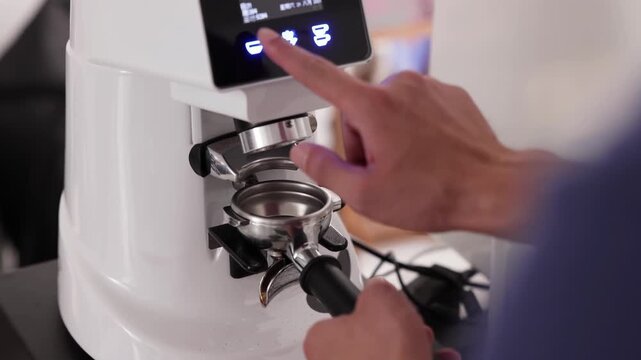 Professional barista or waitress worker pressing the button on electric coffee grinder machine to grind fresh coffee beans powder into portafilter for make espresso hot beverage at coffee cafe shop