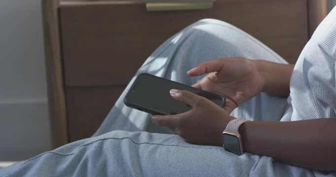 Adult African American woman scrolling phone, lowering to lap, settling to rest at home with watch