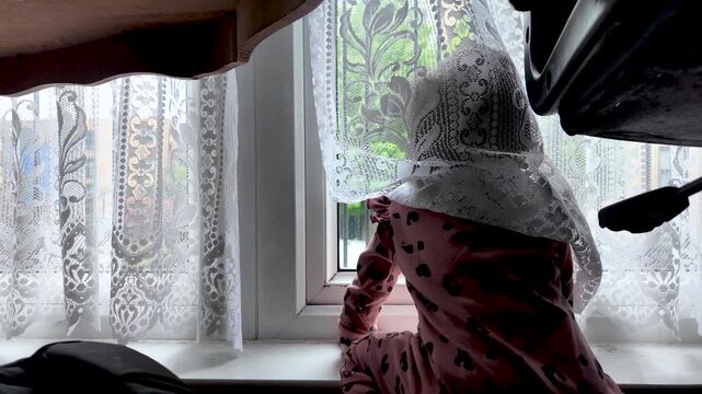 This captures the concept of childhood curiosity and discovery, showing a young South Asian baby looking out a window through delicate lace curtains.