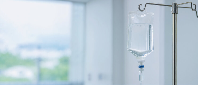 IV drip bag hanging on a metal pole in a hospital room. Intravenous saline solution for patient treatment. Medical infusion therapy concept