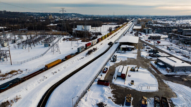 Aerial view of a freight train moving through a snow-covered industrial zone with warehouses and power infrastructure Reading, Ohio, United States.