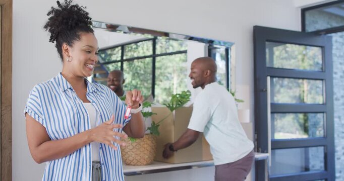 African American couple carrying boxes, woman holding key fob, man clapping, hugging in entryway
