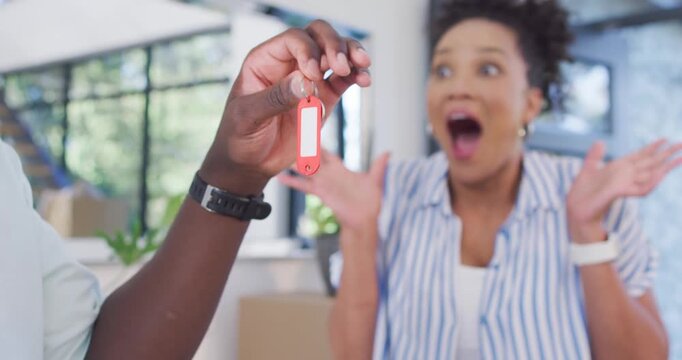 African American couple reacting as man entering left holding red-tag key at new home, her clapping