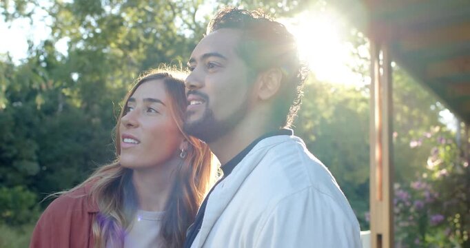 Couple standing on porch edge by wooden post, watching sun flare, turning inward, embracing closely