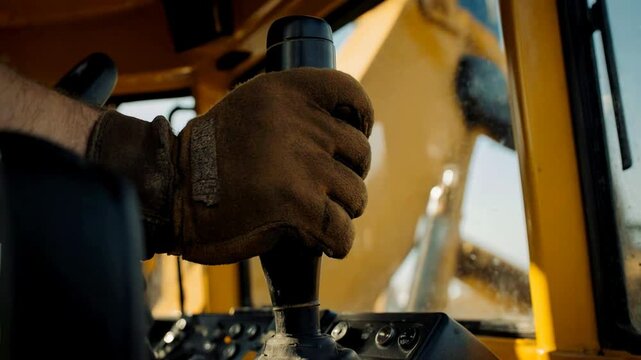 Close-up of a worker hand in a leather glove operating an excavator joystick. Heavy machinery operator controlling equipment inside the cabin