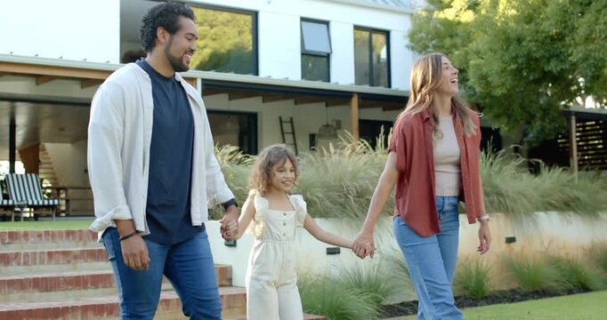 Diverse family with child walking down brick steps from home holding hands, woman pointing to pool