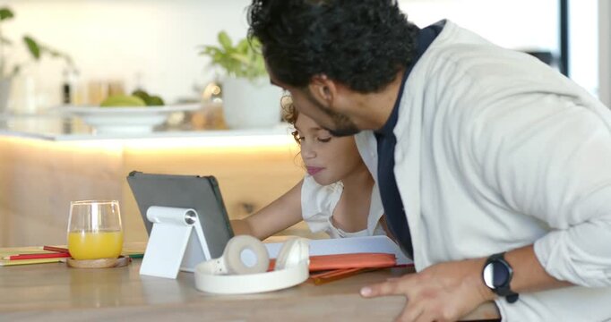 Family father approaching guiding child using tablet and pencil at kitchen counter for homework
