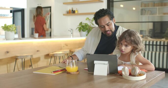 African American dad leaning in guiding school-age daughter at table with tablet and stylus helping
