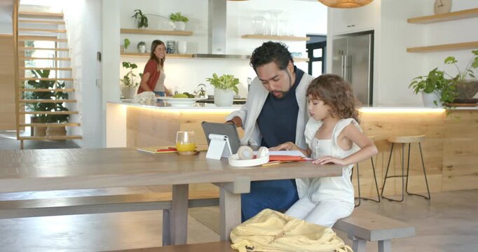 Diverse family father guiding daughter at table using tablet and workbook while mother packing bag