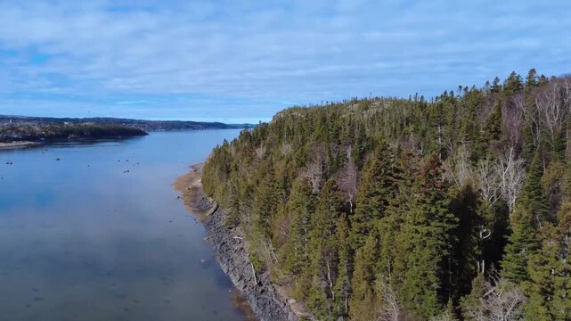 Aerial footage crossing the St. Lawrence River from &Icirc;let Canuel to Rimouski, revealing cloudy skies and the scenic mountain silhouettes of Bic National Park, Quebec landscape.