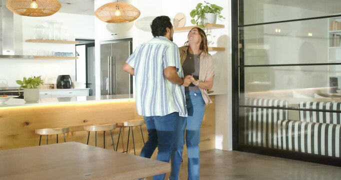 Couple taking hands and dancing near kitchen island, expressing affection, hugging and swaying