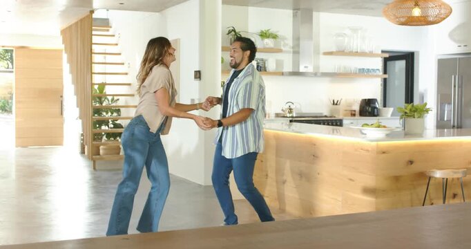 Couple dancing playfully in modern kitchen, woman pulling man toward wood island for fun