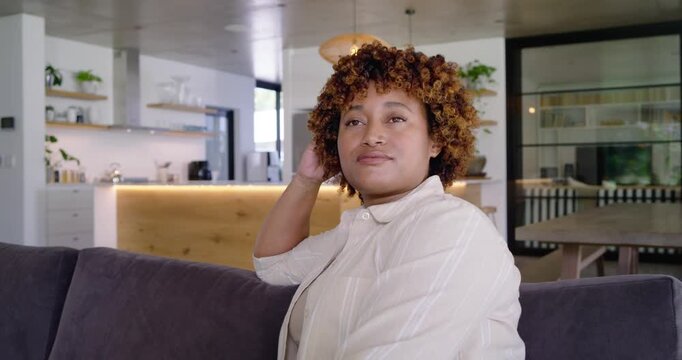 Adult woman reacting off camera touching hair turning head smiling laughing on sofa in open kitchen