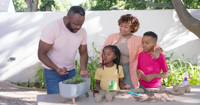 African American family potting at yard table father placing planter spraying green bottle teaching