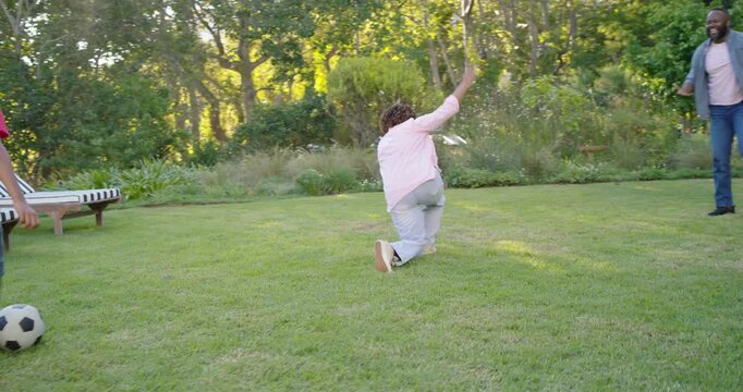 African American family playing soccer casually in backyard, girl dribbling ball, boy challenging