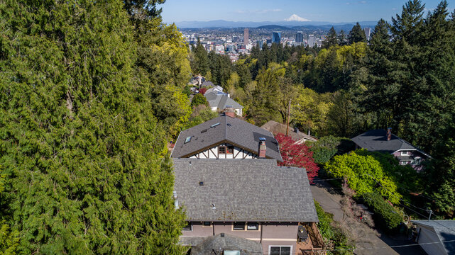 Aerial view of Northwest Imperial Terrace residential rooftops nestled among lush green trees with the Portland skyline and Mount Hood in the distance Portland, Oregon, United States.