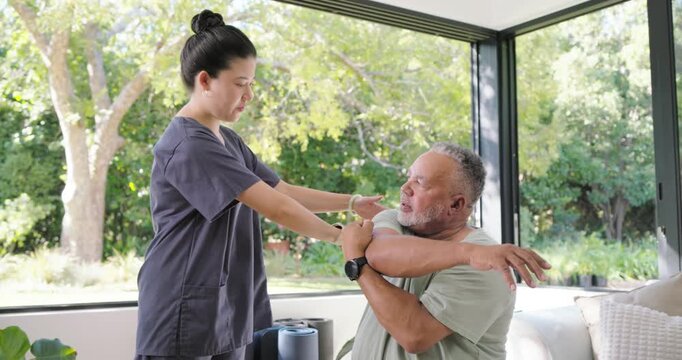 Asian nurse in scrubs giving cues assisting African American man for shoulder mobility near window