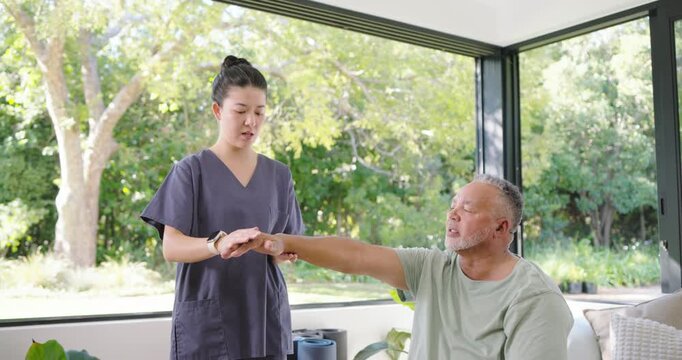 Diverse caregiver in scrubs taking male patient's right wrist at home, guiding motion for checkup